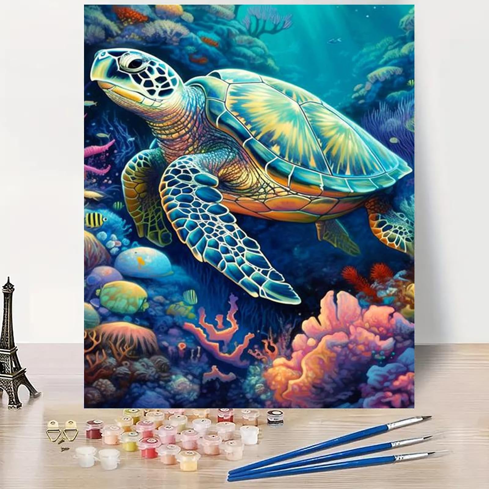 Paint by numbers kit showing a sea turtle swimming among colorful coral and fish, with paint pots and brushes in the foreground.