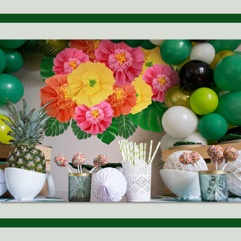 Tropical party setup with colorful paper flowers, palm leaves, balloons, pineapple, and cake pops.