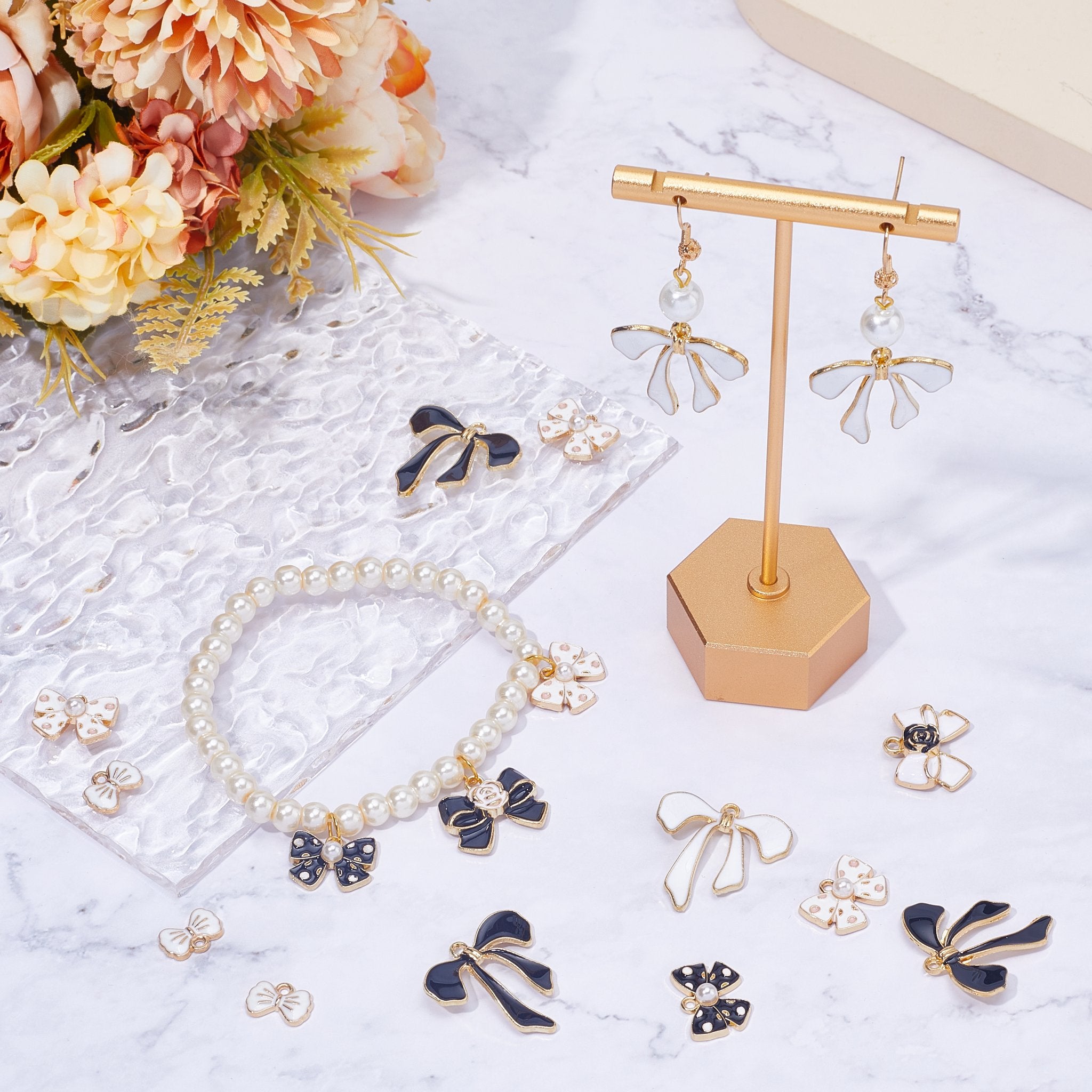 Assortment of pink and black enamel bow charms and a pearl bracelet on a marble surface with flowers