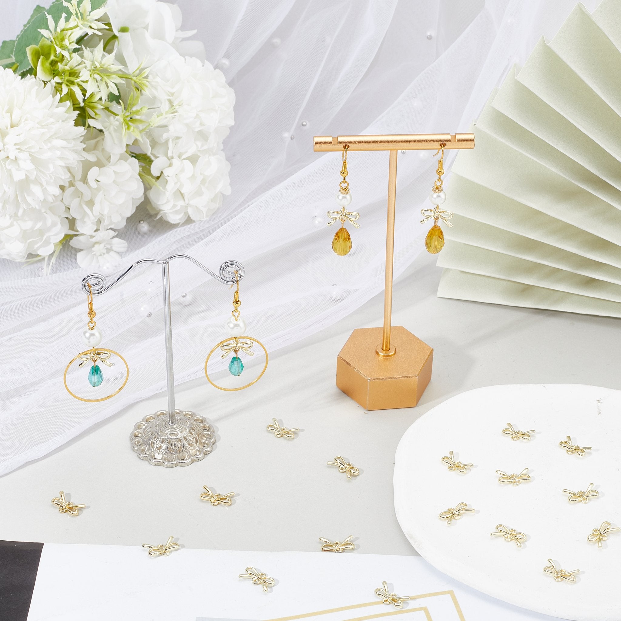 Gold bow charms and finished earrings displayed on a flat surface with decorative elements.