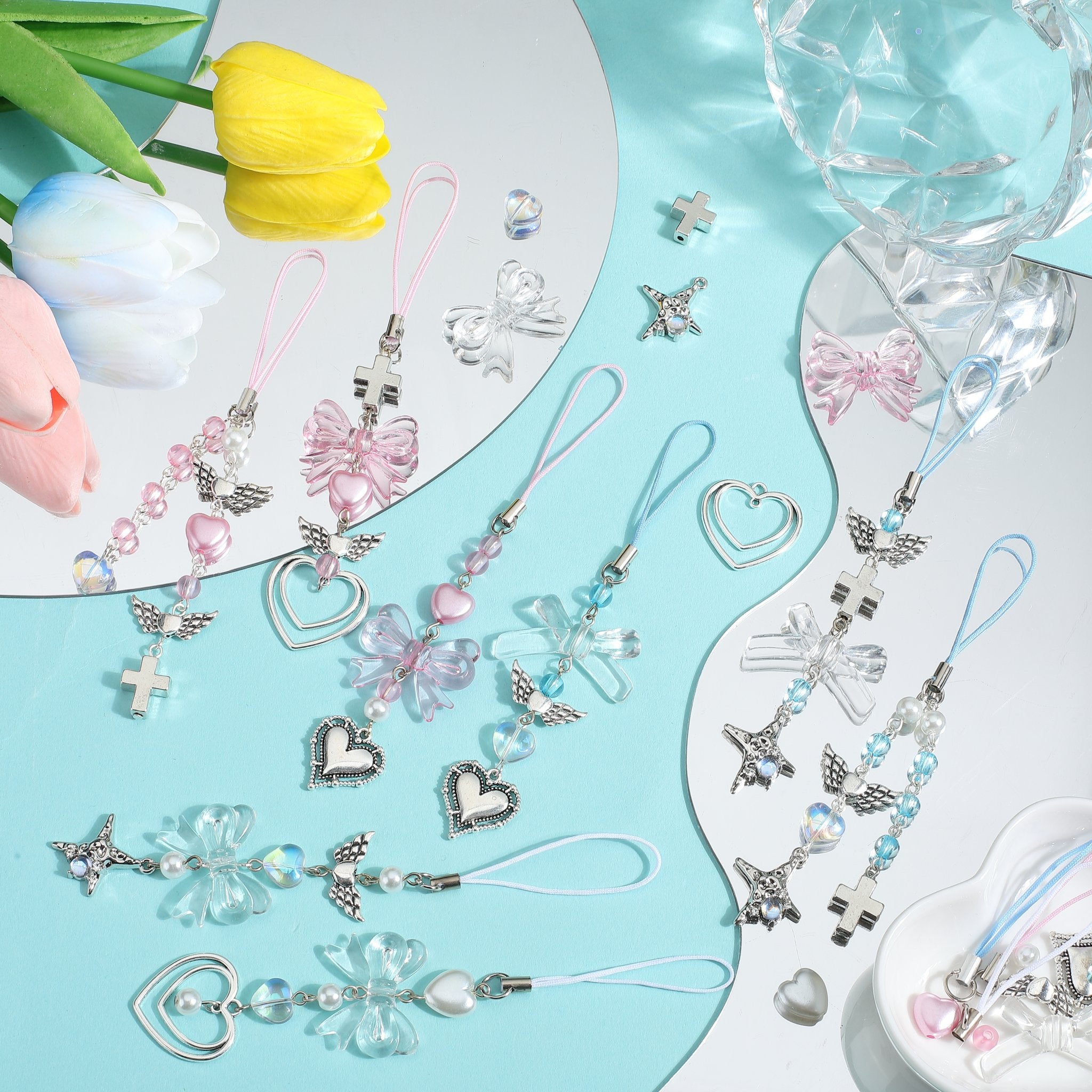 Assortment of pink and clear enamel bow charms with heart and cross pendants for jewelry making, arranged with tulips and crystal decor.