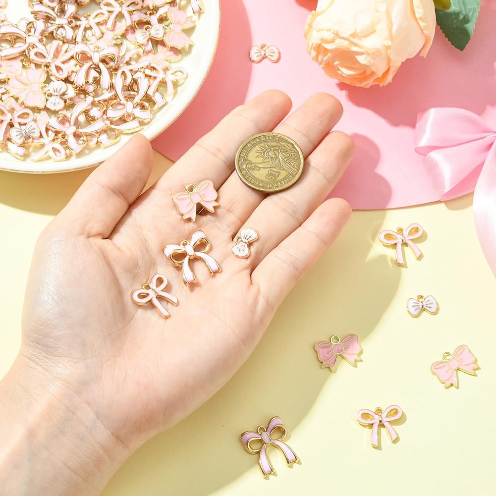 Hand holding pink enamel bow charms with gold trim, a coin for scale, and a bowl of charms in the background.