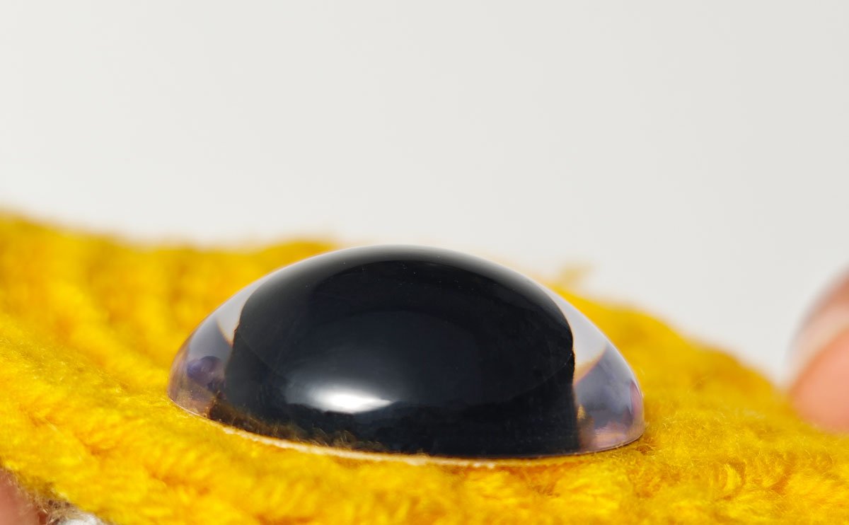 Close-up of a black safety eye with a clear dome, attached to yellow fuzzy material.