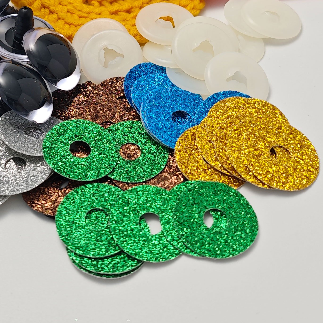 Assorted glitter safety eyes and plastic washers for amigurumi crafts on a white background.