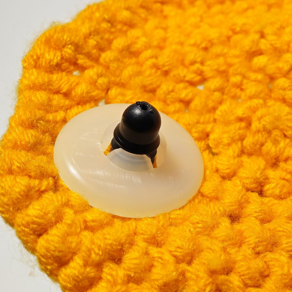 Close-up of a black safety eye post and plastic washer inserted into yellow crochet fabric