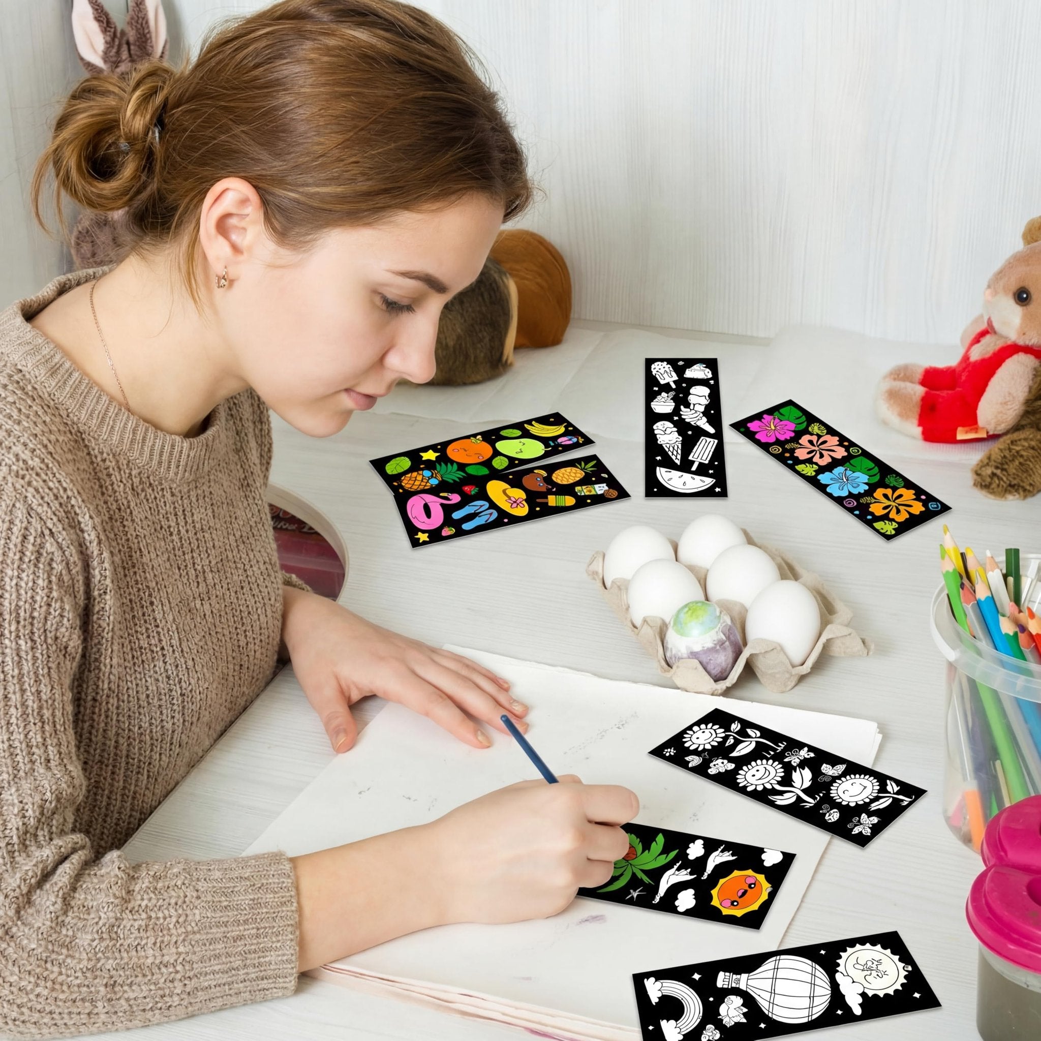 Young woman coloring scratch art bookmarks with summer designs and ribbons