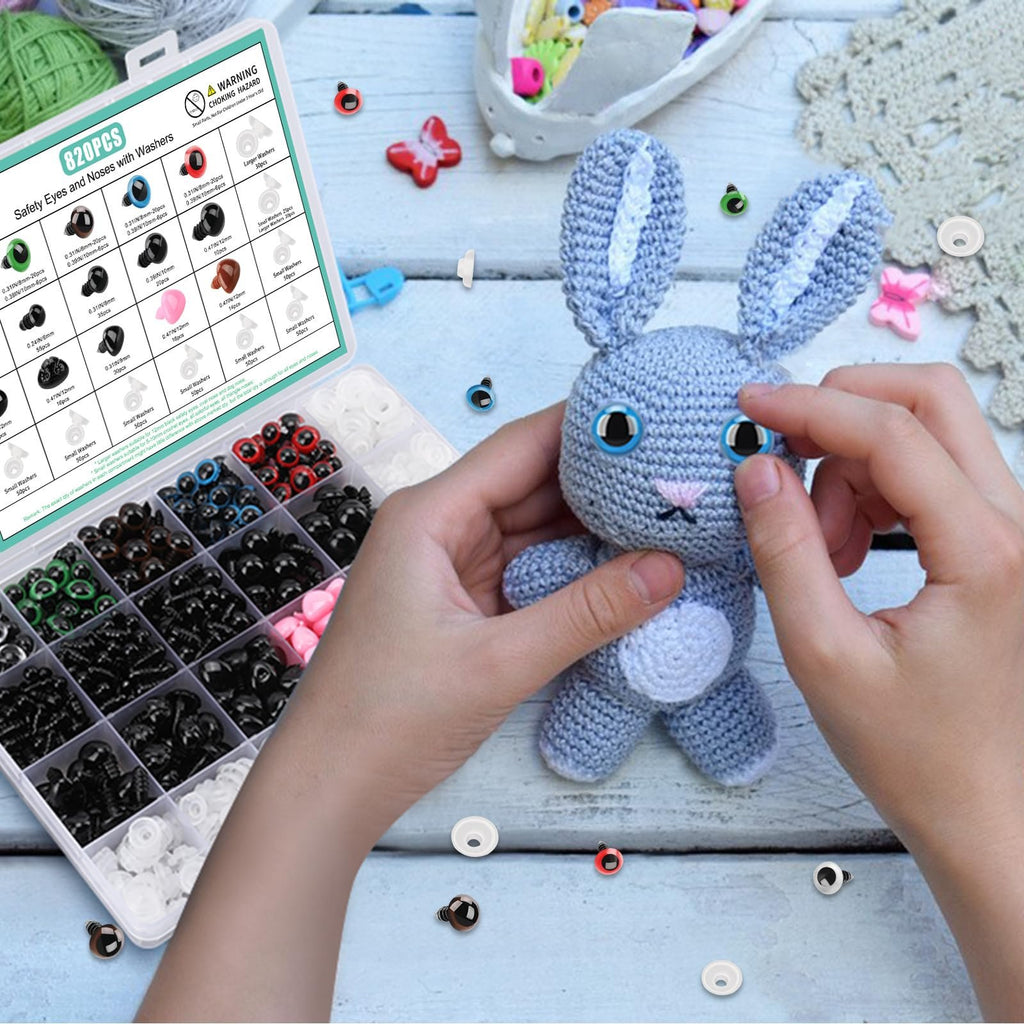 Hands attaching blue safety eyes to a crocheted gray bunny with a kit of eyes and noses open nearby.