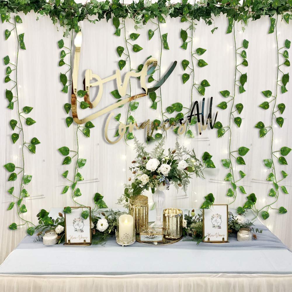 Wedding decor with artificial ivy garlands, a 'Love Congratulates All' sign, and floral arrangements on a table.