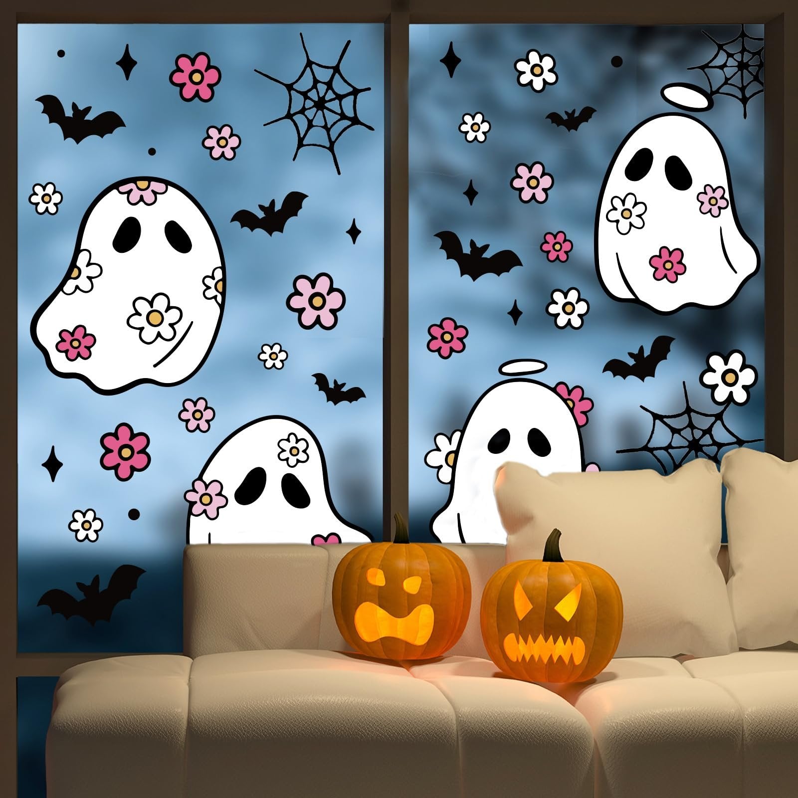 Halloween window clings featuring ghosts, bats, spiderwebs, and flowers applied to a window, with pumpkins and pillows on a couch below.