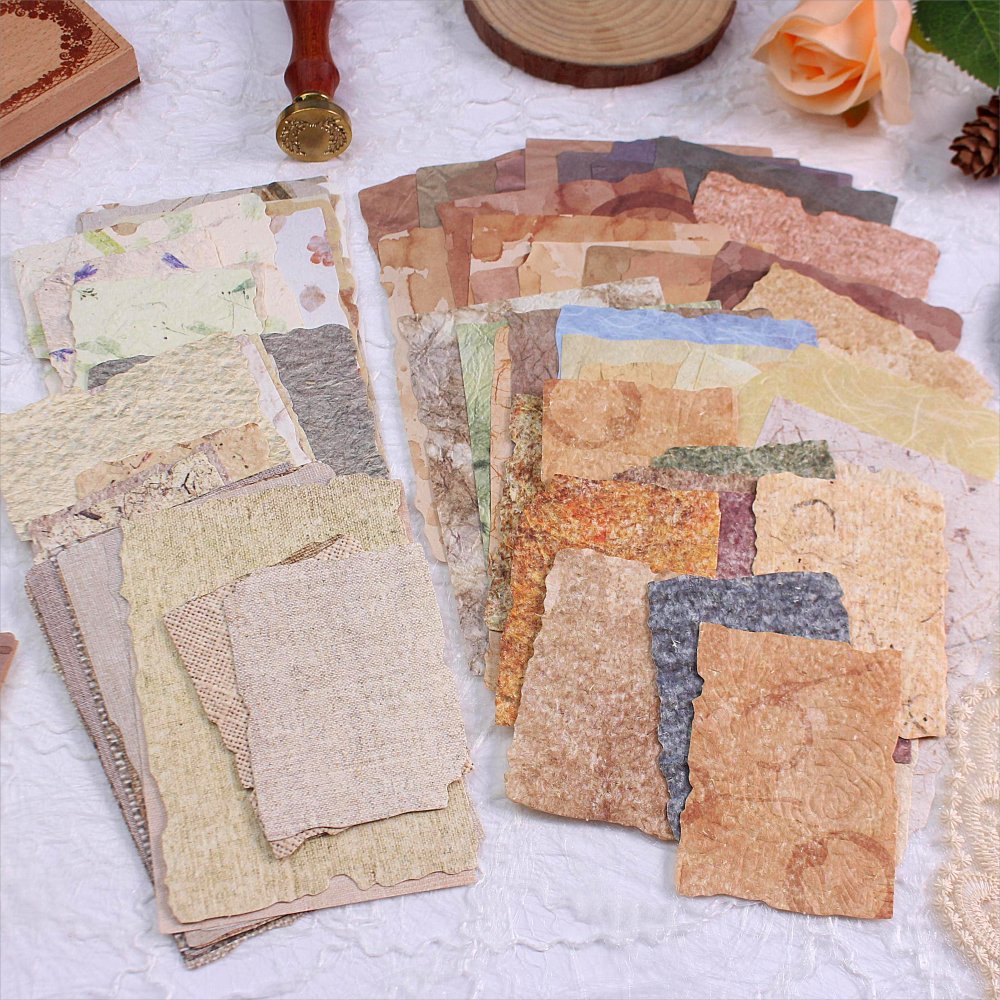 Assortment of textured vintage collage papers with deckled edges, arranged in stacks on a white textured surface.