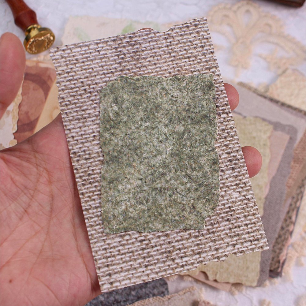 Hand holding textured scrapbook paper samples with deckled edges and embossed patterns.