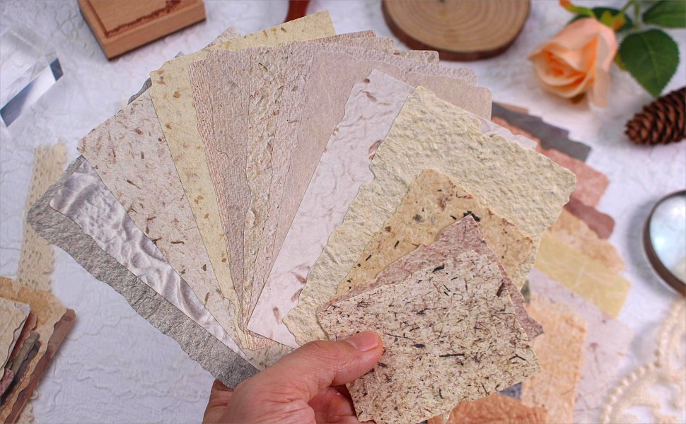 Hand holding a fan of textured scrapbook paper in various neutral tones and deckled edges