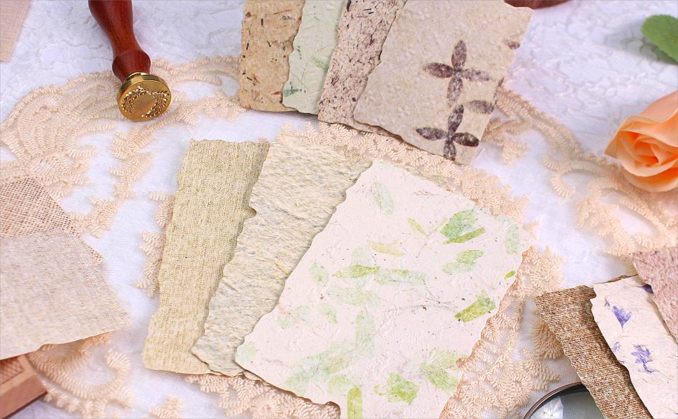 Assortment of textured scrapbook papers with deckled edges, some with floral and leaf imprints, arranged with a wax seal stamp and lace.