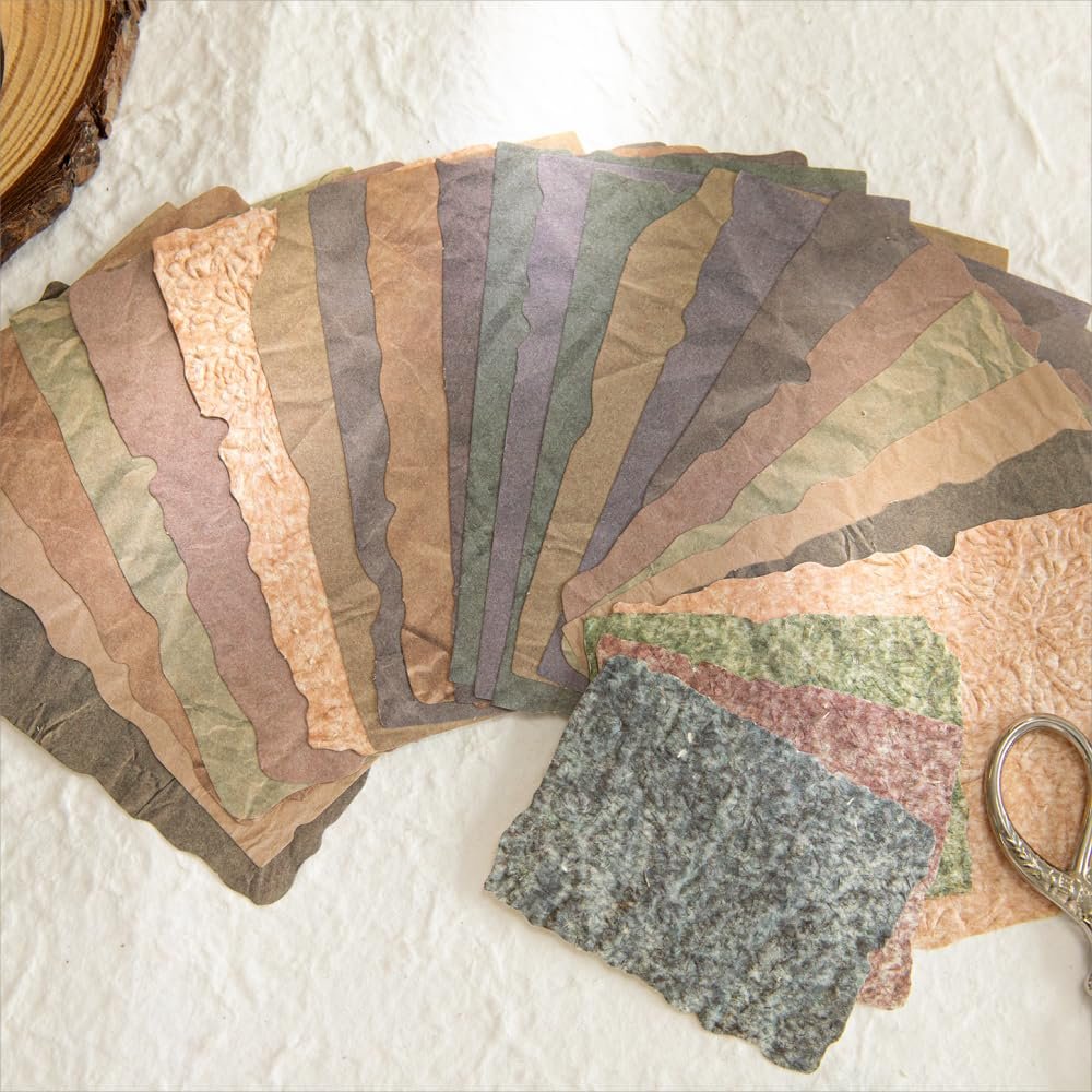Fan of textured scrapbook paper in various earthy tones and deckled edges, with a few smaller pieces and scissors in the foreground.