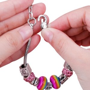 Hands connecting a snake chain charm bracelet with colorful beads and silver charms