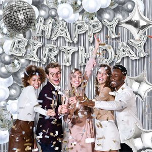 Group of five people celebrating with champagne and confetti, surrounded by silver birthday decorations including balloons and a disco ball.