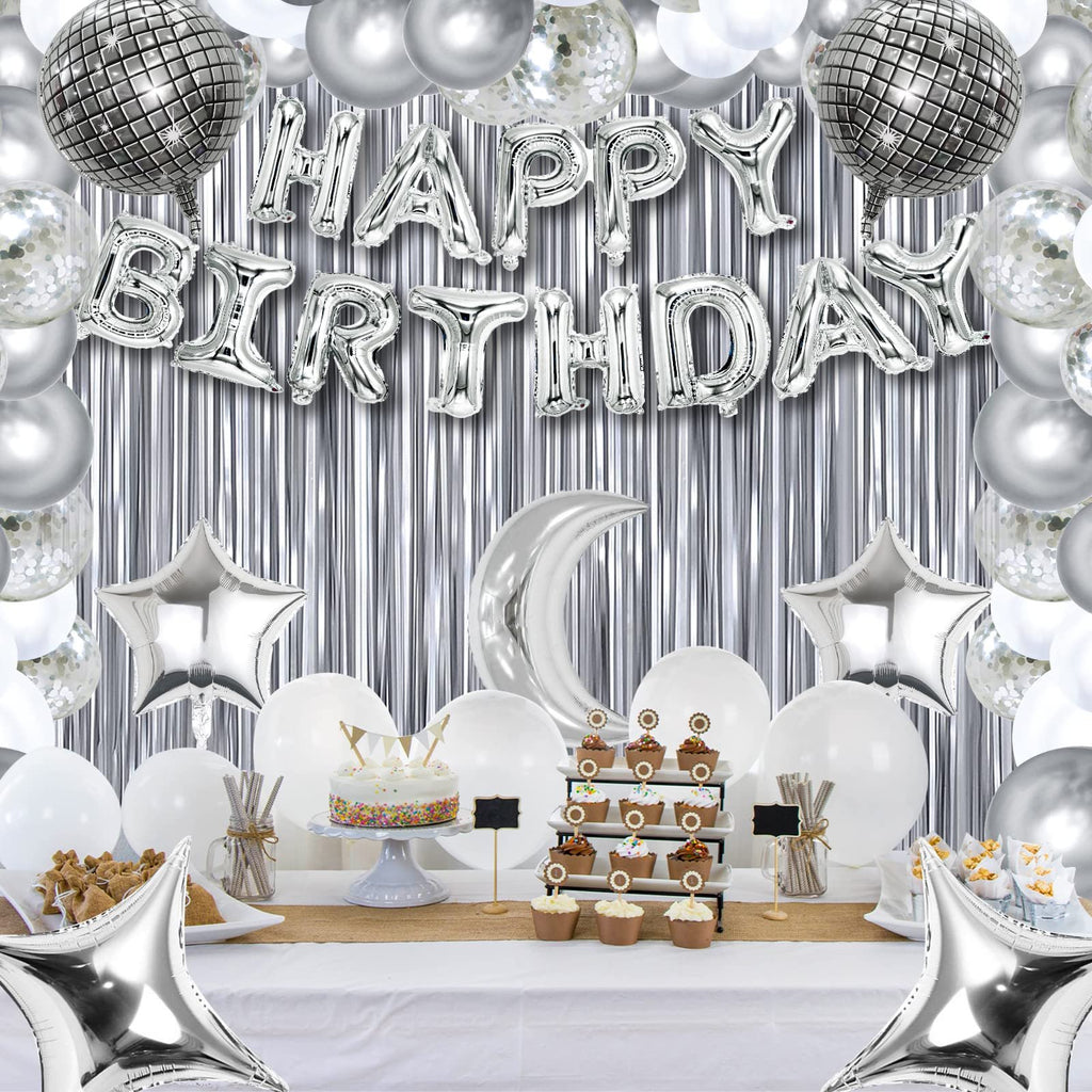 Silver and white birthday party decorations including balloons, a cake, cupcakes, and a metallic fringe backdrop.