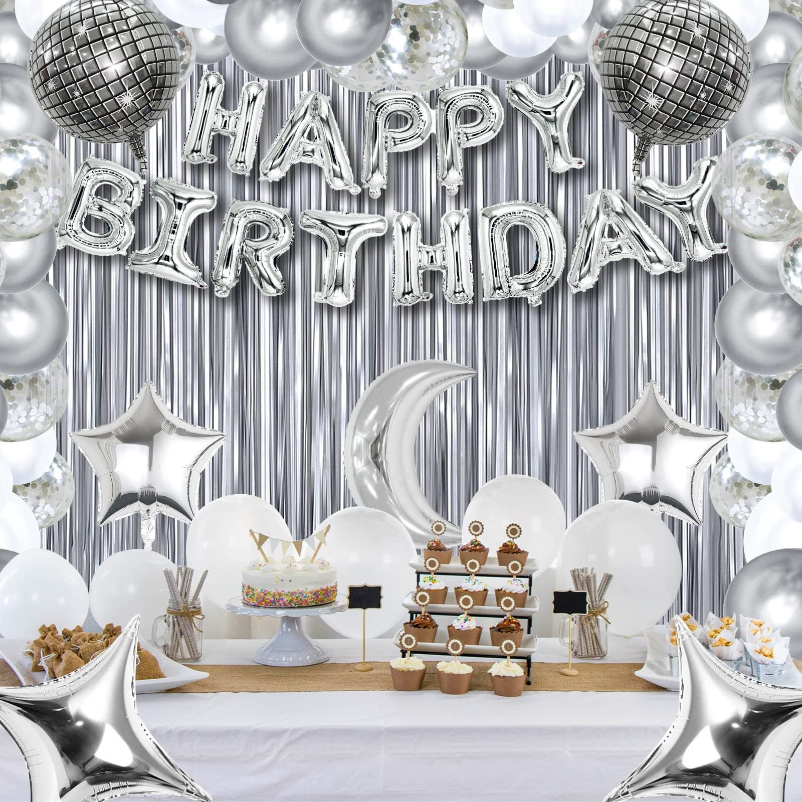 Silver and white birthday party decorations including balloons, a cake, cupcakes, and a metallic fringe backdrop.