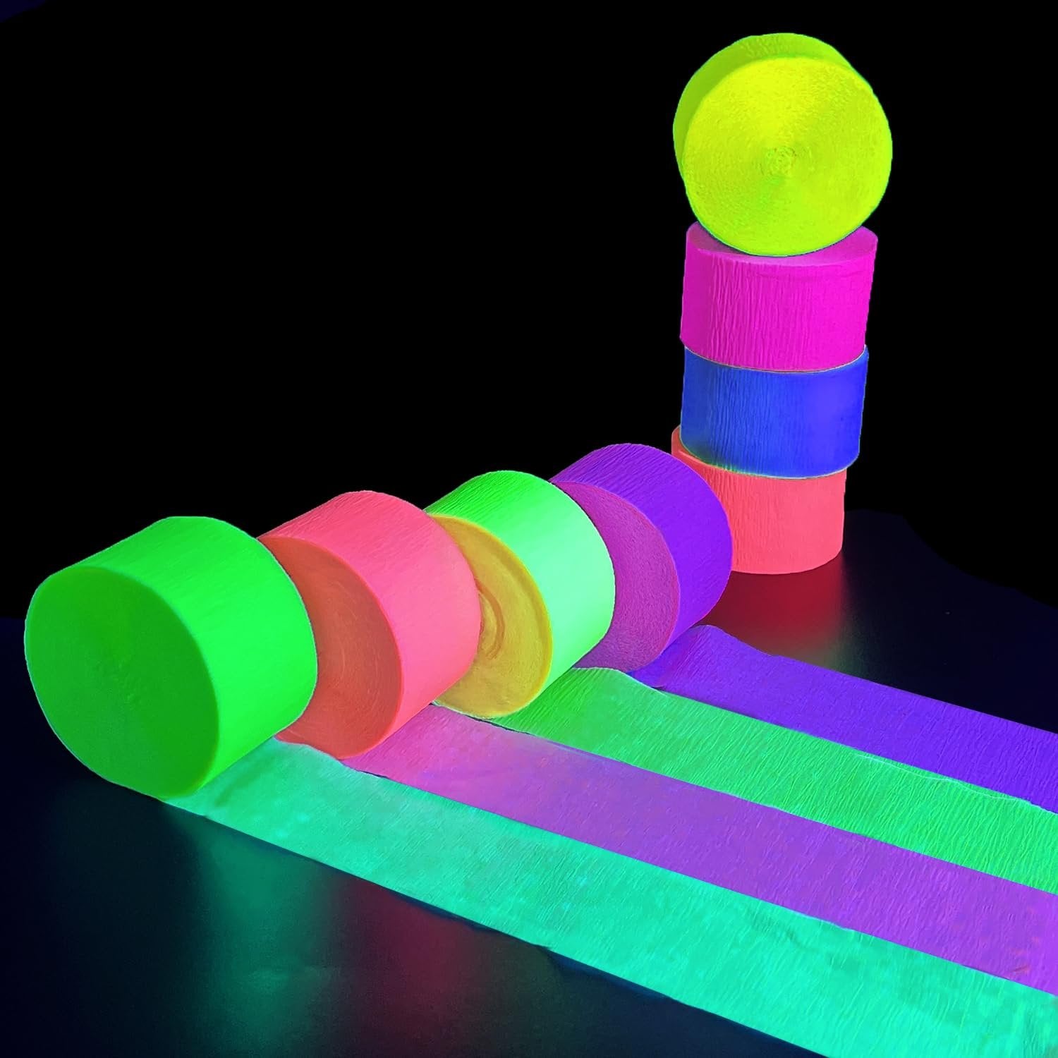 Stack of neon crepe paper streamer rolls and unrolled streamers glowing under blacklight