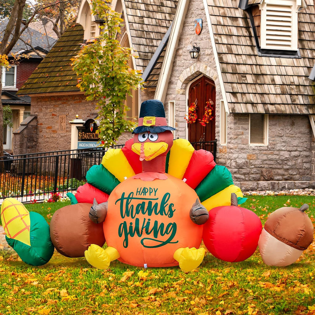 Inflatable Thanksgiving turkey with vegetables and 'Happy Thanksgiving' text, set up on a lawn in front of a stone building.