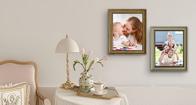Two rustic farmhouse picture frames displaying family photos, hung on a wall above a table with a lamp and flowers.