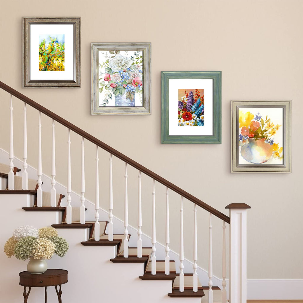 Four framed floral watercolor prints displayed on a wall next to a staircase with a vase of flowers on a side table.
