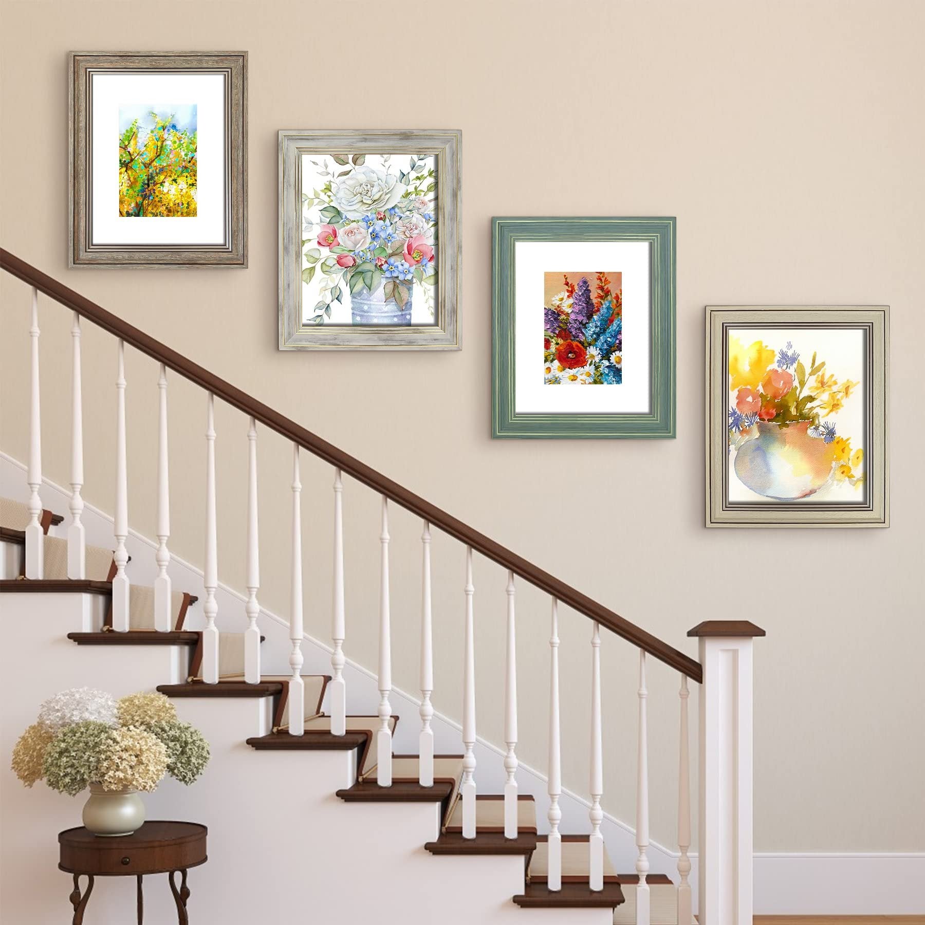 Four framed floral watercolor prints displayed on a wall next to a staircase with a vase of flowers on a side table.