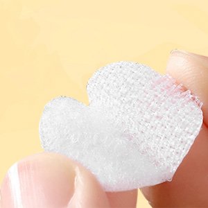 Close-up of a white heart-shaped adhesive dot with hook-and-loop fastener, held between two fingers.