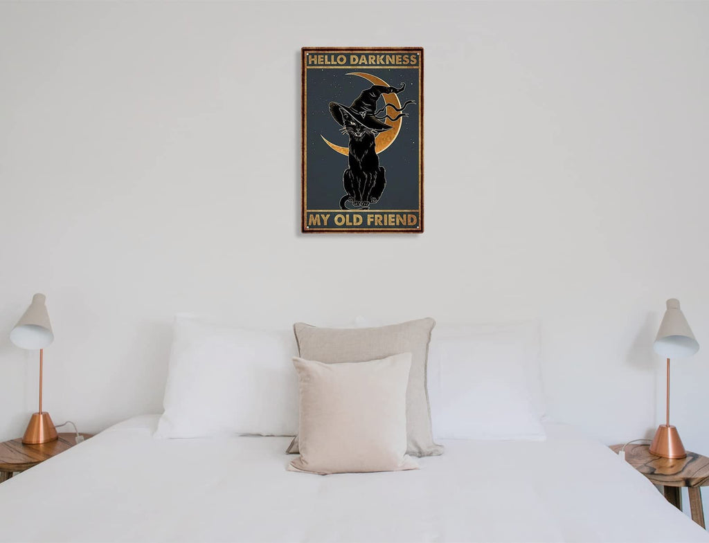 Black cat wearing a witch hat sits in front of a crescent moon on a tin sign that reads 'Hello Darkness My Old Friend'.