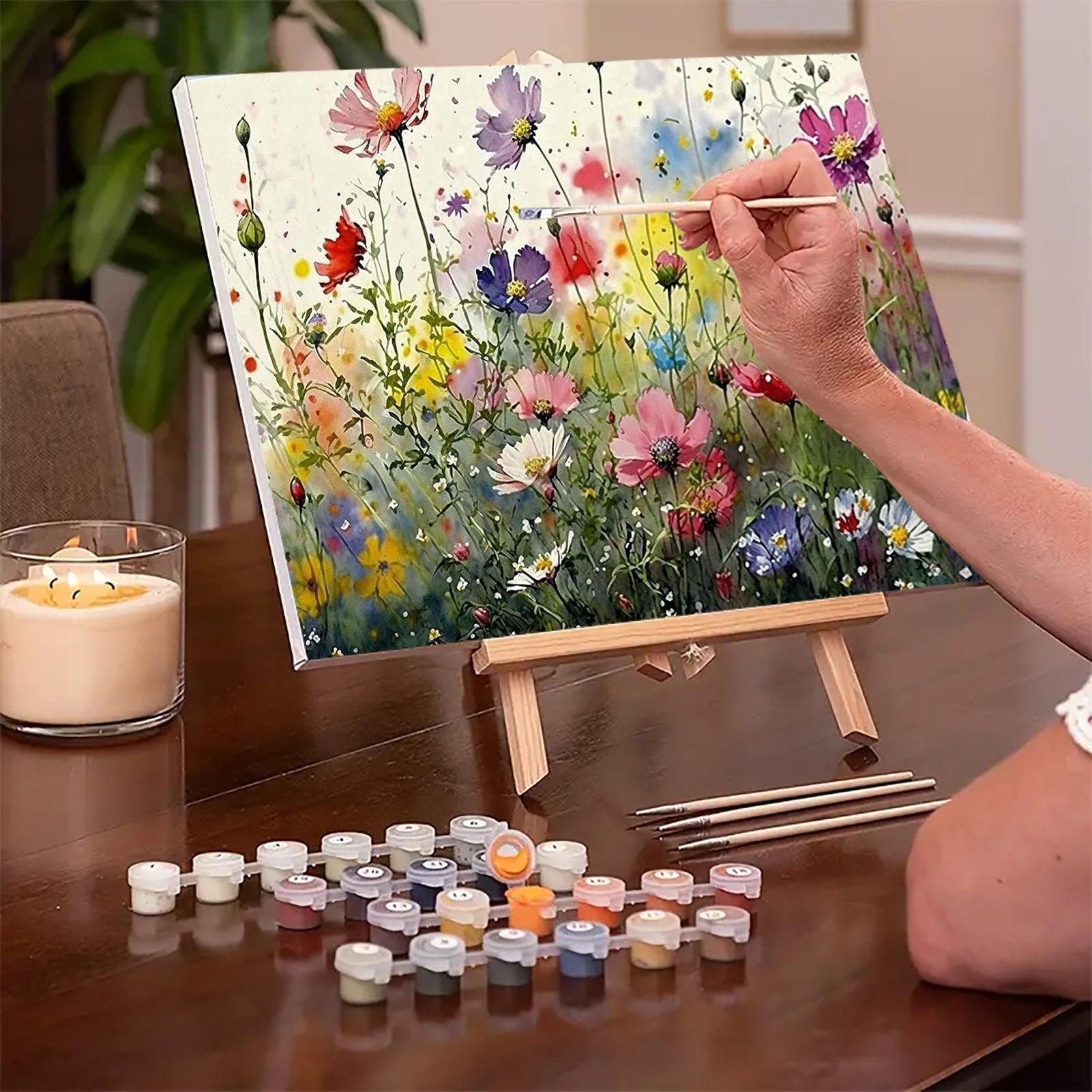 Person painting a floral scene on canvas with acrylic paints and brushes on a wooden easel.
