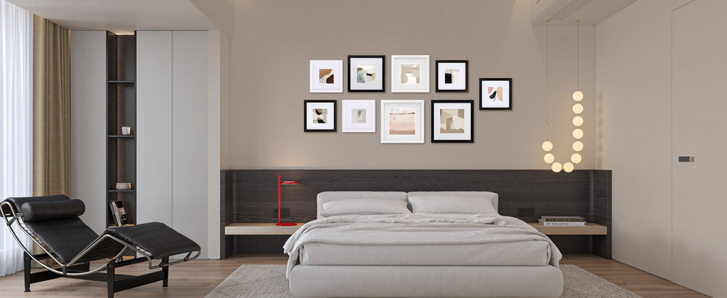 Bedroom scene with a wall of seven framed abstract art prints above a bed, a chaise lounge, and a nightstand.