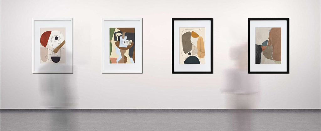 Four framed abstract art prints displayed on a white wall, two with white frames and two with black frames.