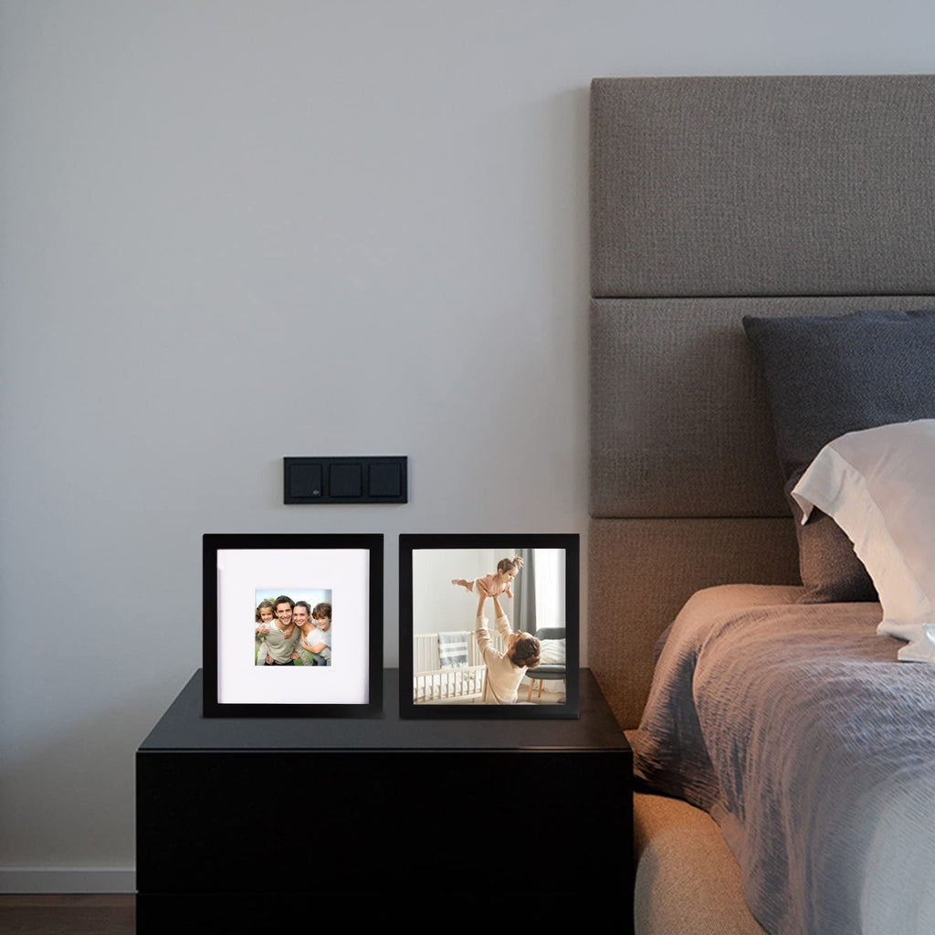 Two black picture frames on a nightstand next to a bed, one showing a family, the other a parent with a baby.