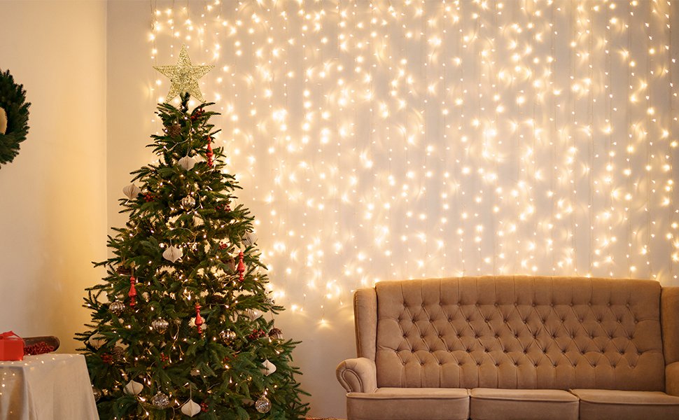 Decorated Christmas tree with a gold star topper, set against a wall of warm fairy lights and a tufted sofa.