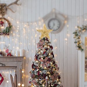 Gold 5-point star Christmas tree topper on a decorated tree in a festive room setting.