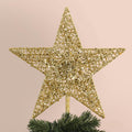 Gold glitter 5-point star Christmas tree topper on faux pine branches, close-up view