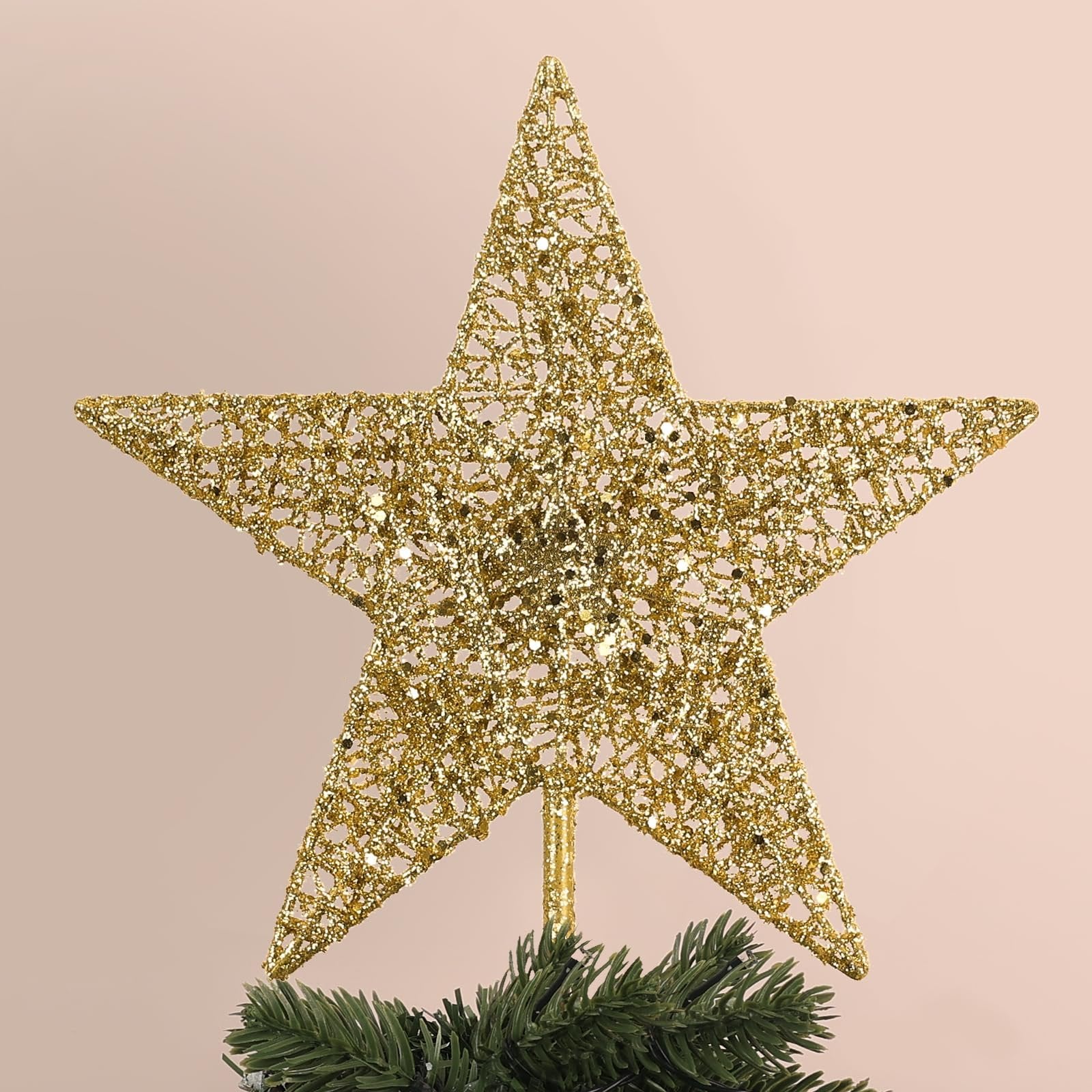 Gold glitter 5-point star Christmas tree topper on faux pine branches, close-up view