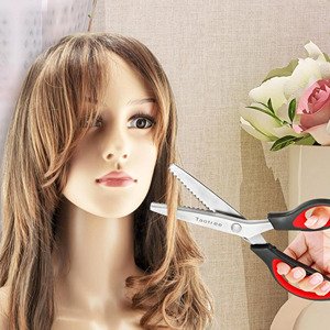 Pinking shears with zigzag teeth and soft-grip handles being held near a mannequin's hair