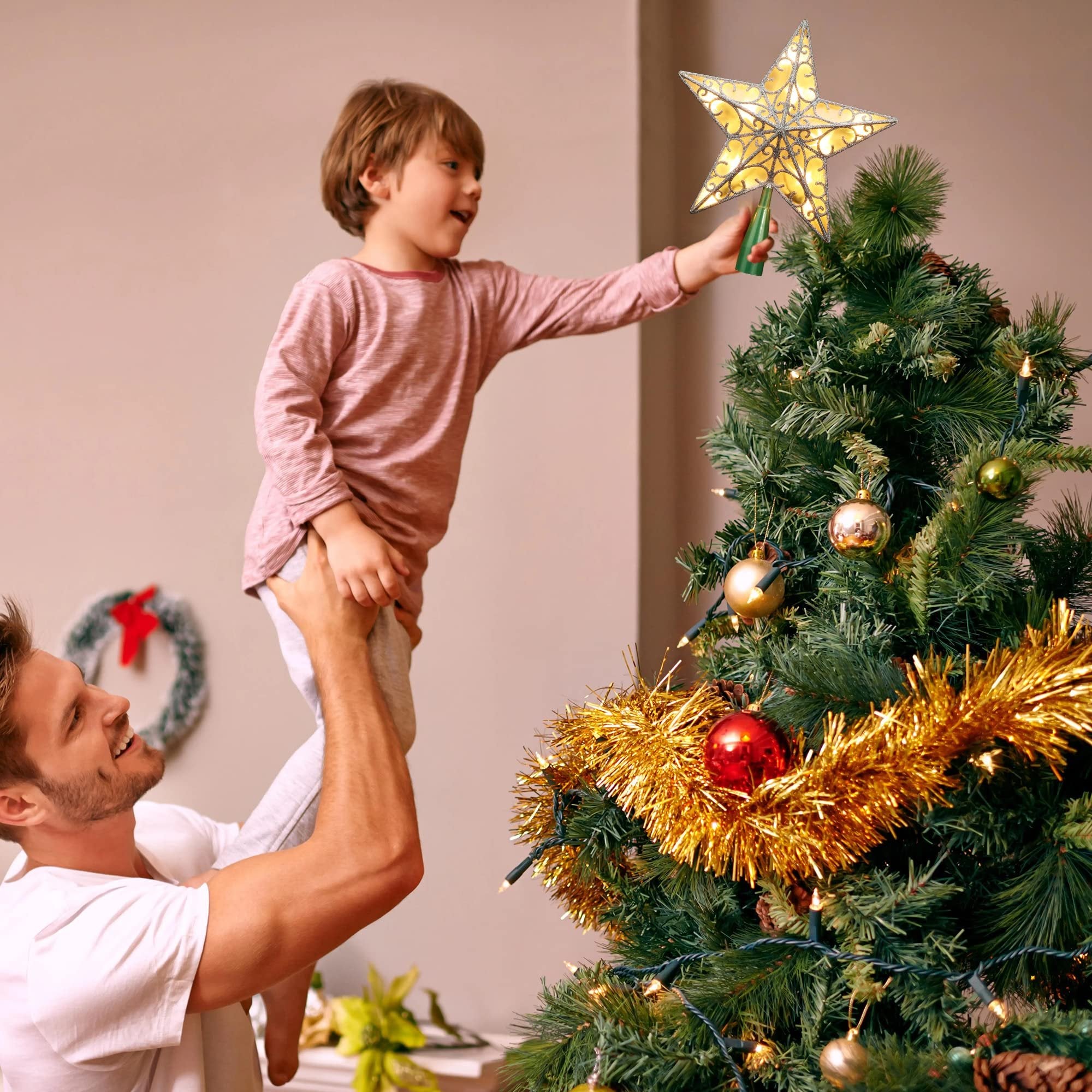 Father holding son to place a glittery star tree topper with warm white lights on a decorated Christmas tree