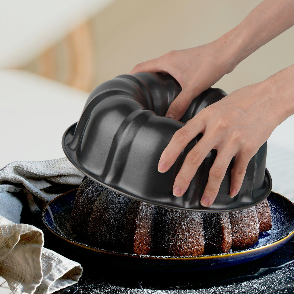Hands removing a fluted tube cake pan from a bundt cake dusted with powdered sugar.