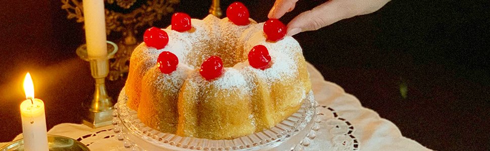Fluted tube cake dusted with powdered sugar and topped with cherries, presented on a cake stand with lit candles nearby.