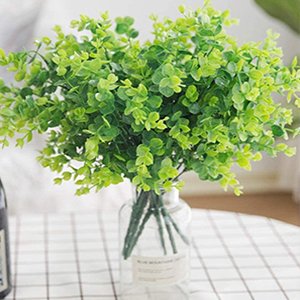 Artificial boxwood greenery stems in a clear glass vase on a checkered surface