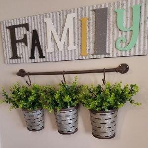 Three galvanized metal planters with artificial boxwood greenery hanging on a wall with a 'FAMILY' sign above.