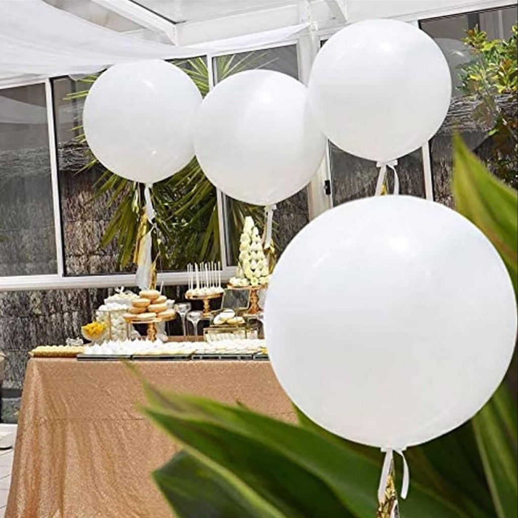 Four large white latex balloons floating above a dessert table at an outdoor event.