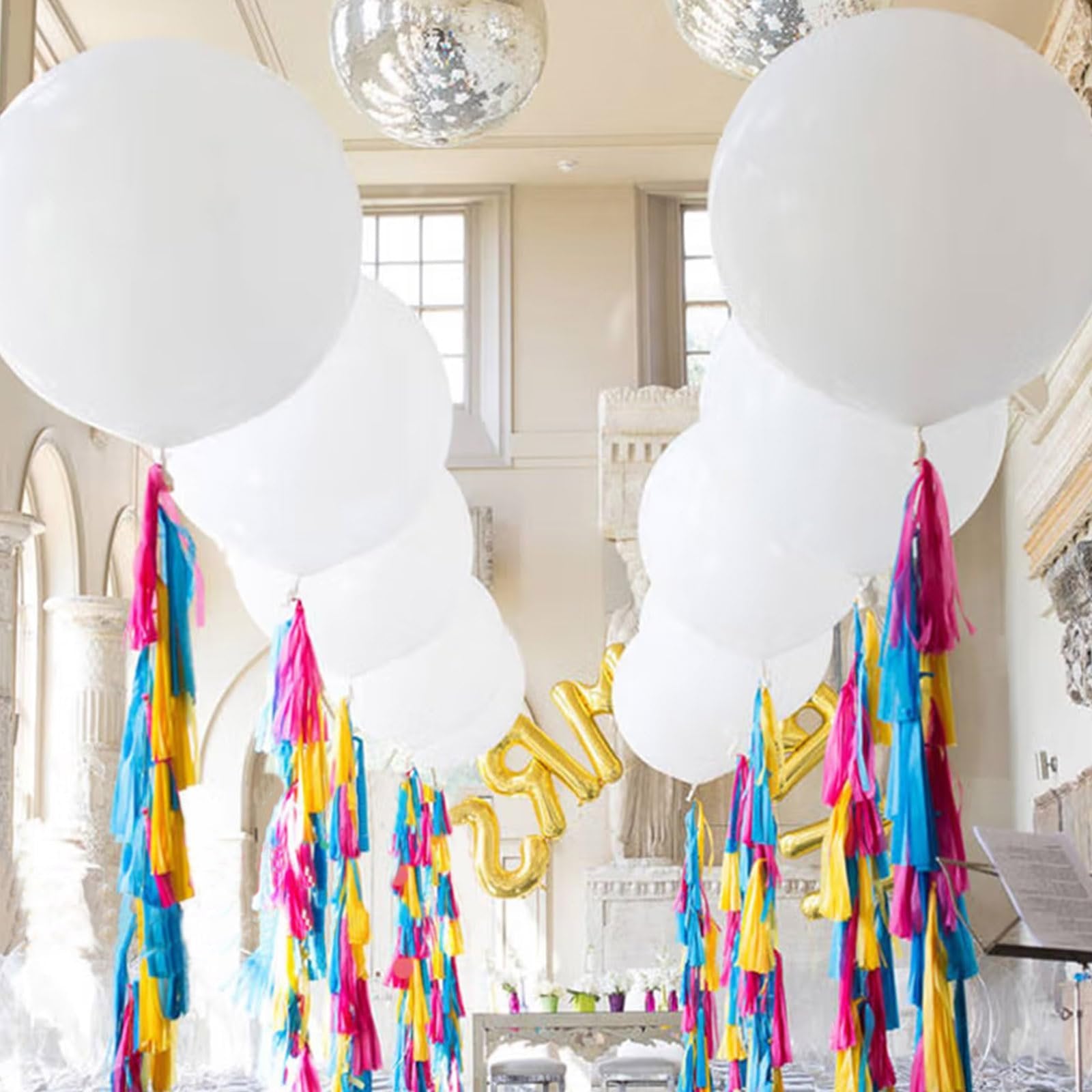 Large white balloons with colorful tassels hanging in a room with disco balls and gold letter balloons.