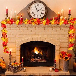Fall maple leaf garland with warm orange lights draped over a brick fireplace mantel with candles and decorations.