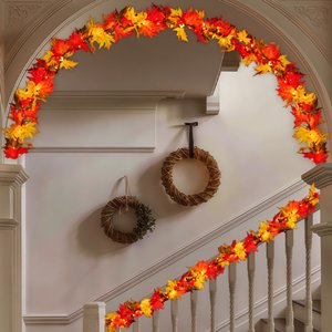 Fall maple leaf garland with warm orange lights draped over a staircase railing and archway