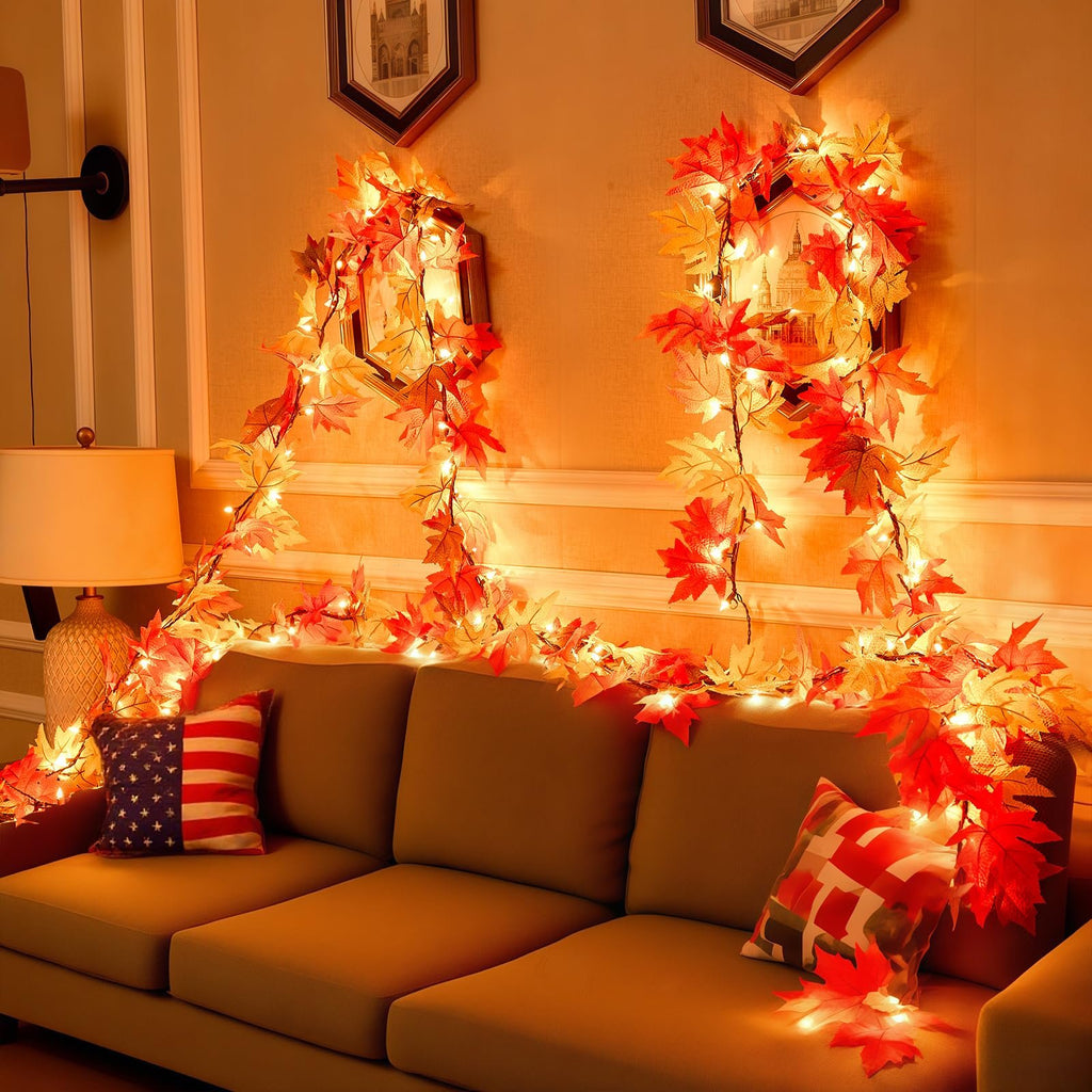 Fall maple leaf garland with warm orange lights draped over a sofa with decorative pillows.