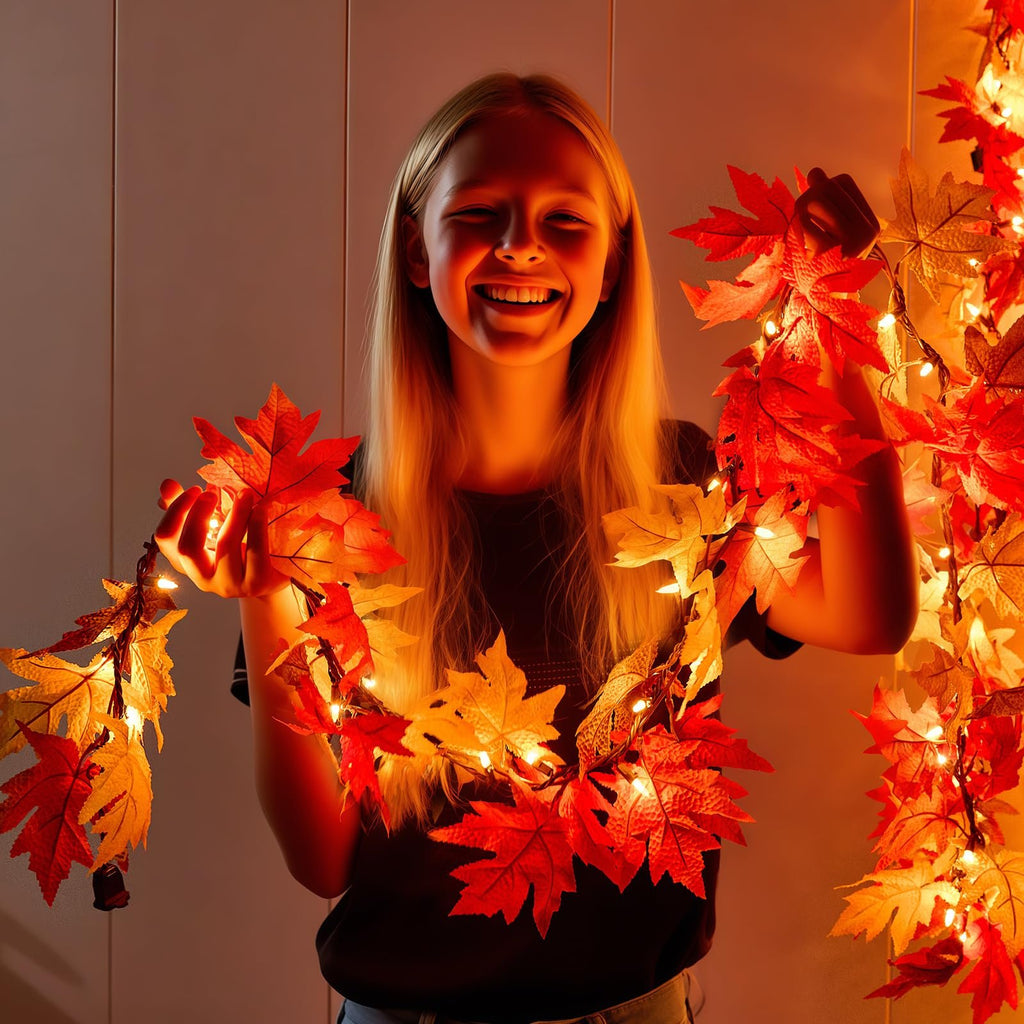 Smiling girl holding a string of artificial maple leaves with warm orange lights