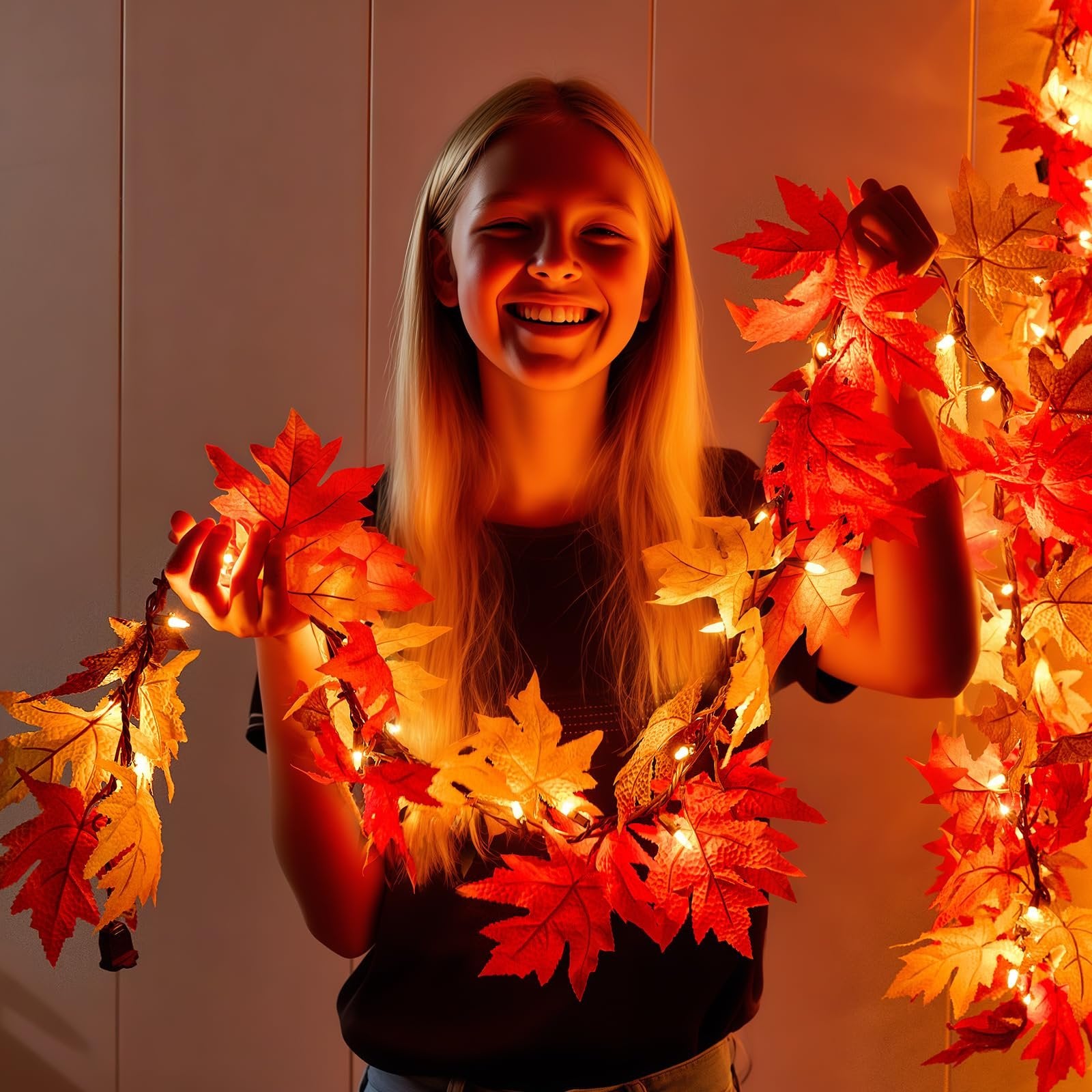 Smiling girl holding a string of artificial maple leaves with warm orange lights